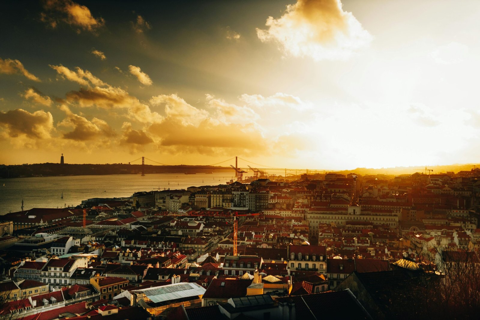 A beautiful view of Lisbon at sunrise with the Tagus River and iconic bridge in sight.