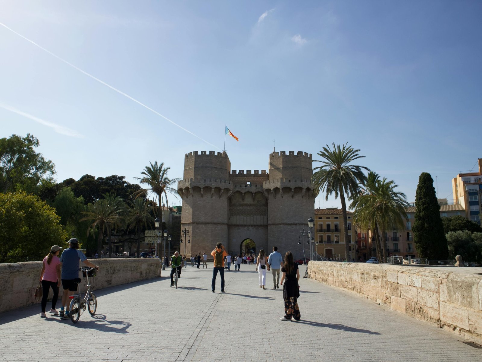 Tourists explore the historic Torres de Serranos under a bright blue sky in Valencia, Spain.