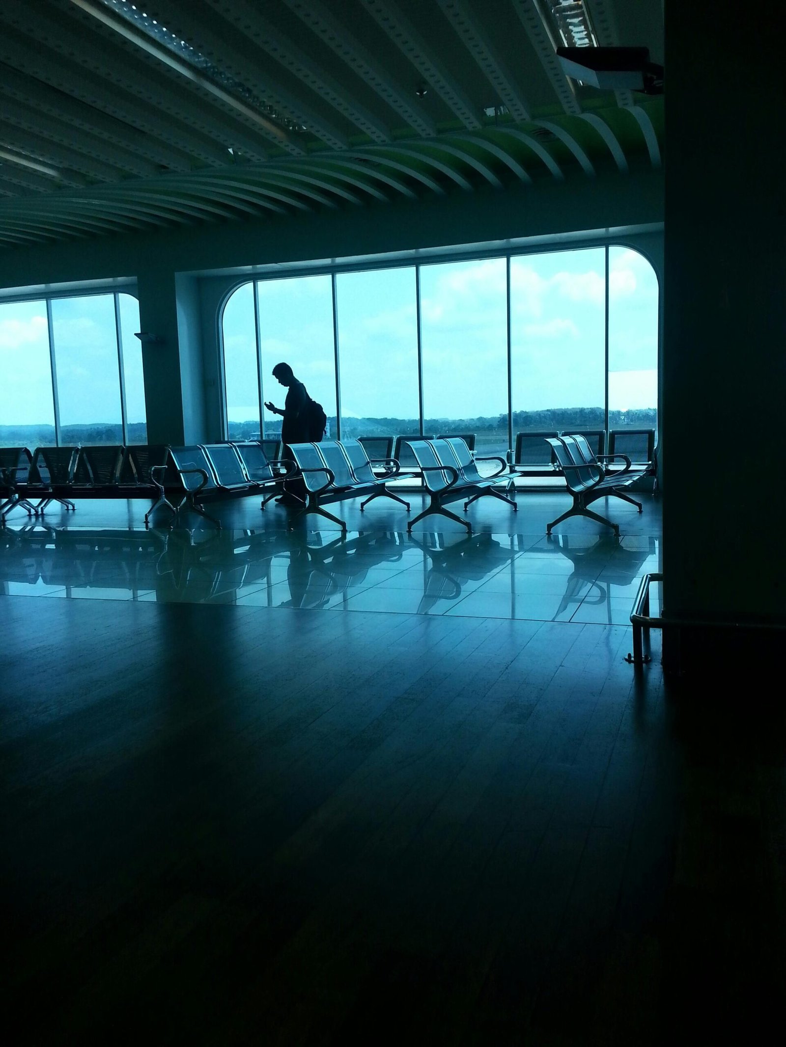A silhouette of a person waiting at an airport terminal with large windows and seating.