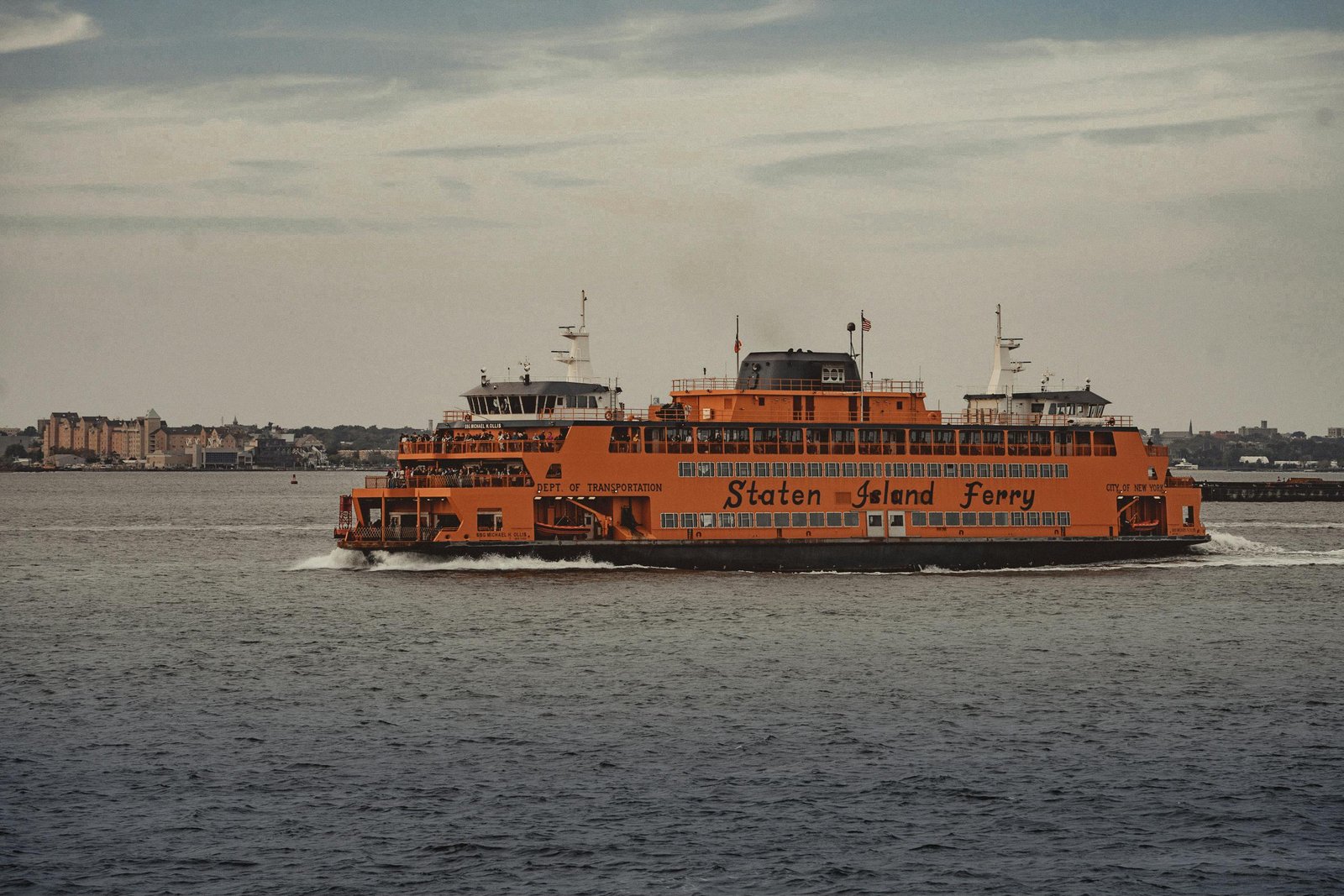 A Staten Island Ferry transporting passengers across New York Harbor with cityscape in the background.