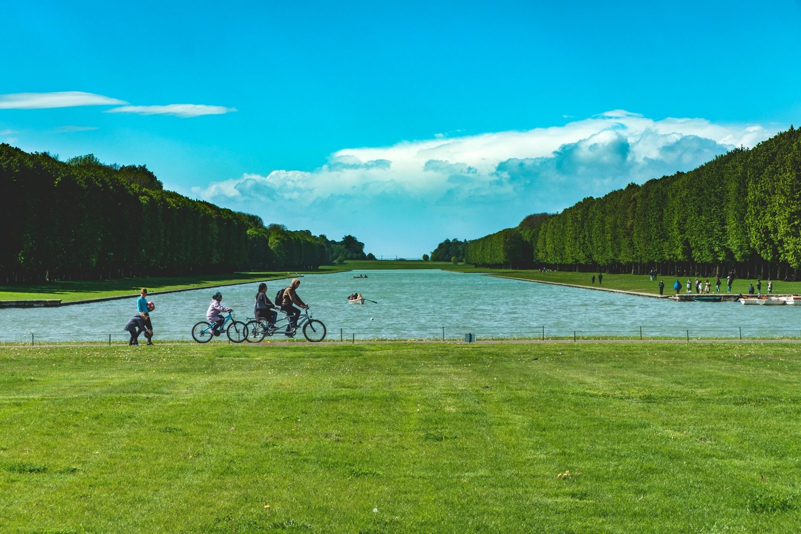 People biking and walking by the Grand Canal in Versailles on a sunny day.