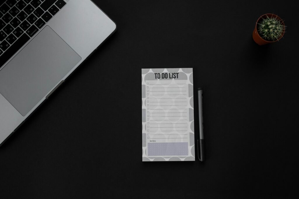 A minimalistic desk setup featuring a laptop, to-do list, and pen on a dark background. Ideal for productivity themes.